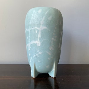 May include: A light blue ceramic vase with a white crackle glaze pattern. The vase has a rounded body and four short legs.