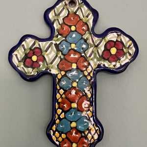 May include: A blue and white ceramic cross with a floral design. The cross is decorated with red, yellow, and blue flowers.