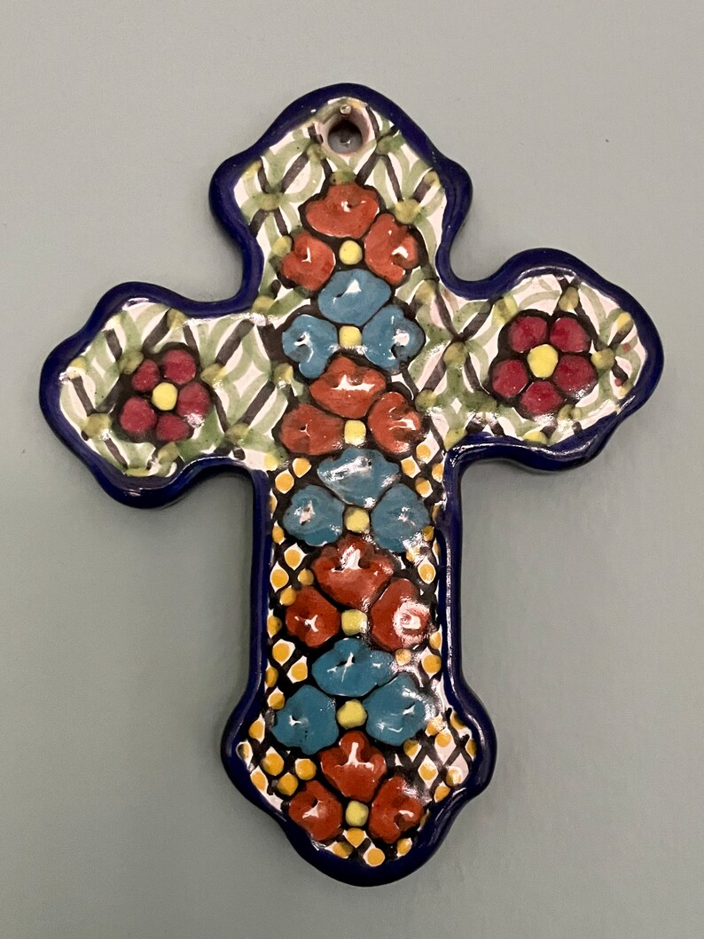 May include: A blue and white ceramic cross with a floral design. The cross is decorated with red, yellow, and blue flowers.