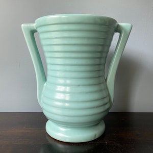 May include: A light blue ceramic vase with two handles and a ribbed design.