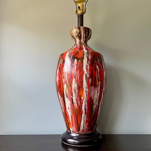 May include: A red, white, and brown ceramic table lamp with a black base. The lamp has a unique, abstract pattern.