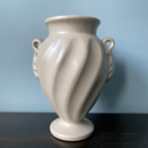 May include: A white ceramic vase with a swirl design and two handles. The vase has a classic, elegant style.