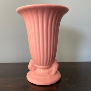 May include: A pink ceramic vase with a fluted design and a decorative base. The vase is approximately 6 inches tall.