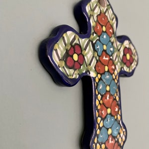 May include: A blue ceramic cross with a colorful floral design. The cross is decorated with red, yellow, blue, and green flowers.