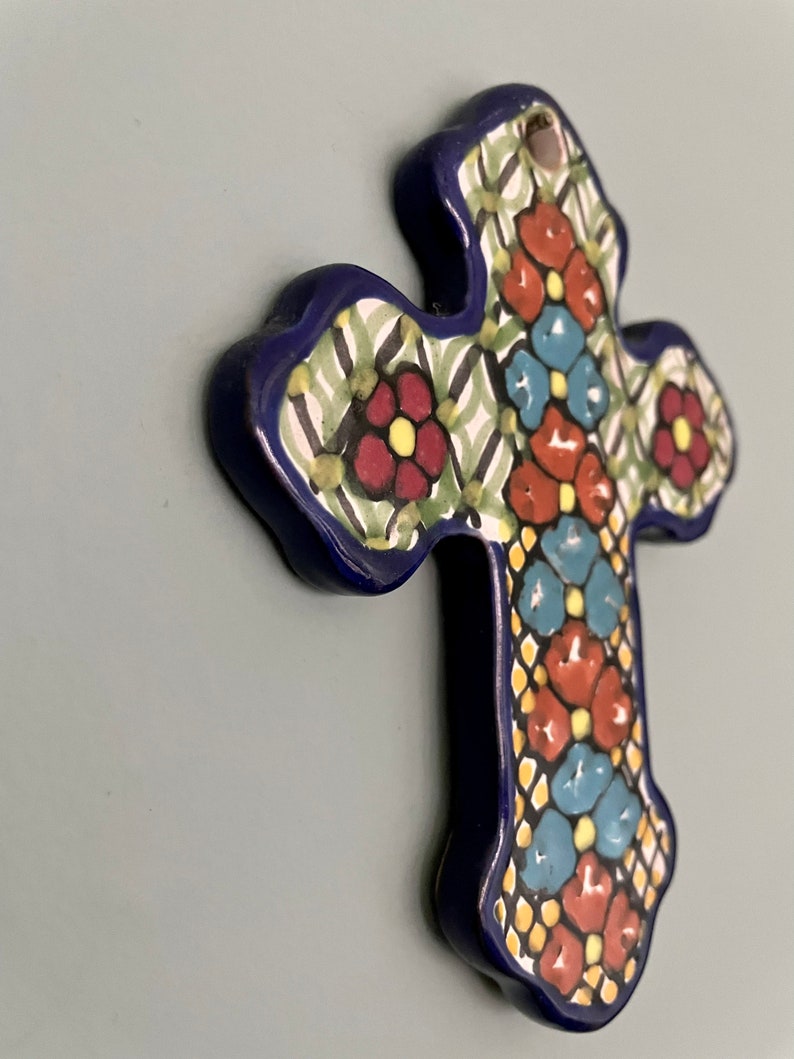 May include: A blue ceramic cross with a colorful floral design. The cross is decorated with red, yellow, blue, and green flowers.