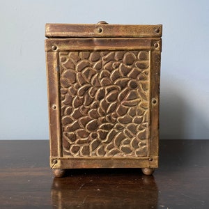 May include: A vintage brass box with a textured, floral design. The box has a hinged lid and sits on four small feet.