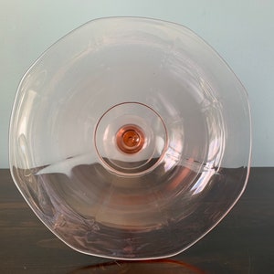 May include: A clear glass cake stand with a pink tint and a scalloped edge. The stand has a raised center base.