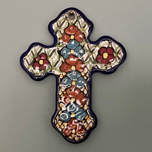 May include: A blue and white ceramic cross with a floral design. The cross is decorated with red, yellow, and blue flowers.