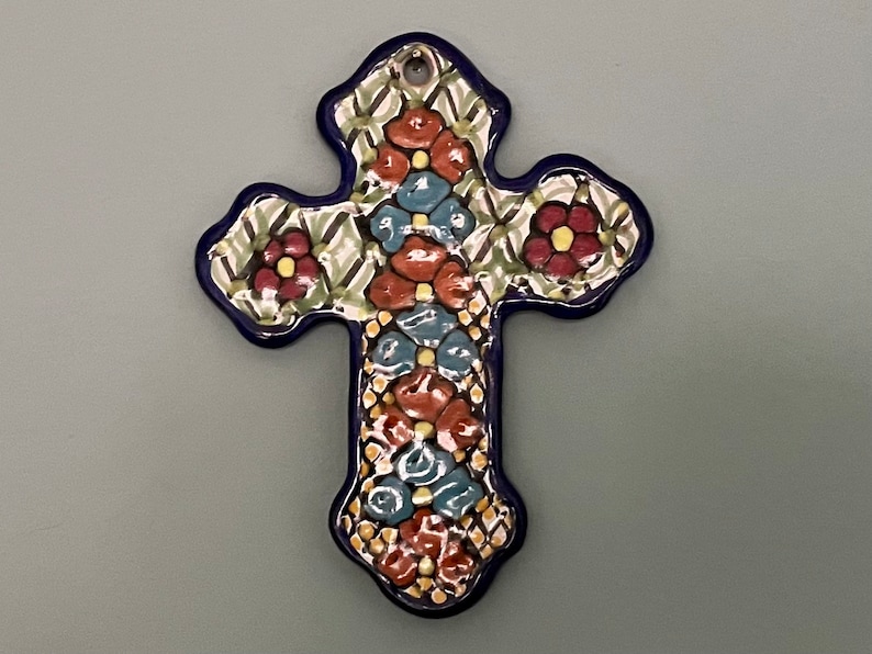 May include: A blue and white ceramic cross with a floral design. The cross is decorated with red, yellow, and blue flowers.
