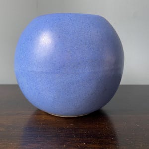 May include: A small, round, light blue ceramic vase with a textured surface.
