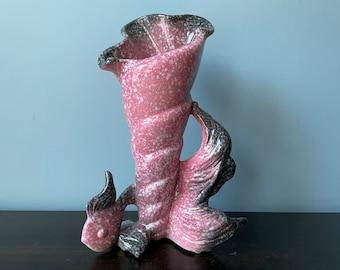 May include: A pink and black ceramic vase shaped like a fish. The vase has a speckled glaze and a wide opening at the top.