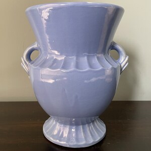 May include: A light blue ceramic vase with two handles. The vase has a fluted design and a round base.