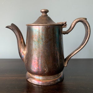 May include: A silver teapot with a tarnished finish. The teapot has a rounded body and a curved handle.