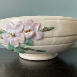 May include: A white ceramic bowl with a floral design. The bowl has a raised rim and a wide base. The flowers are in shades of pink, green, and brown.