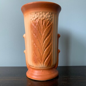 May include: A brown and cream ceramic vase with a floral design and a textured surface. The vase has two handles on the sides.
