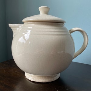 May include: A white ceramic teapot with a lid and a handle. The teapot has a textured surface and a slightly rounded shape.