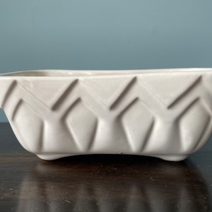 May include: White ceramic planter with a geometric design. The planter has a rectangular shape with a slightly rounded bottom.