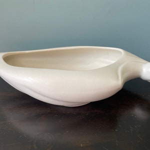 May include: A white ceramic planter shaped like a banana with a rounded handle. The planter is smooth and has a glossy finish.