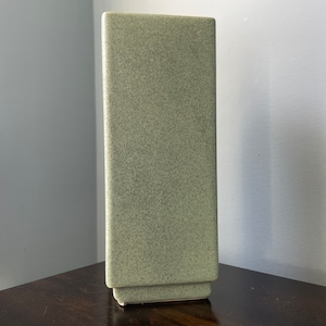 May include: A tall, rectangular vase with a light green speckled glaze.