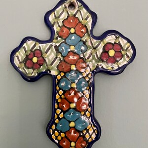 May include: A blue and white ceramic cross with a floral design. The cross is decorated with red, yellow, and blue flowers.