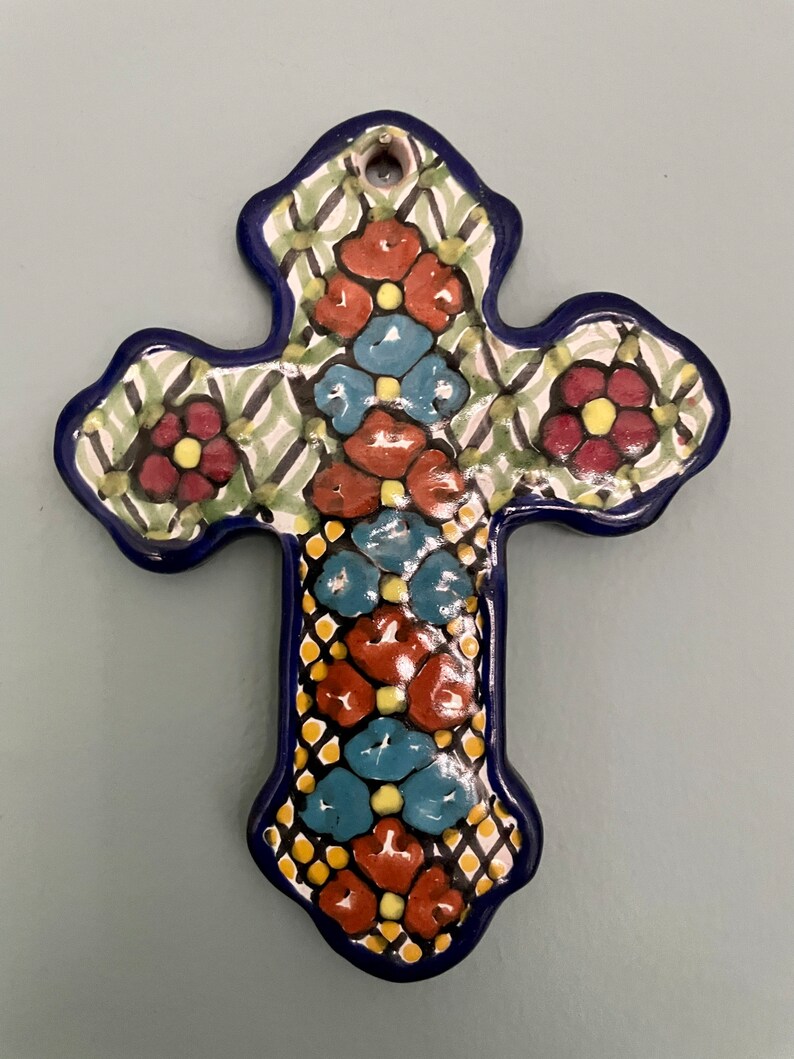 May include: A blue and white ceramic cross with a floral design. The cross is decorated with red, yellow, and blue flowers.