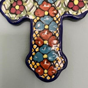 May include: A blue and white ceramic cross with a floral design. The cross is decorated with red, blue, yellow, and green flowers.