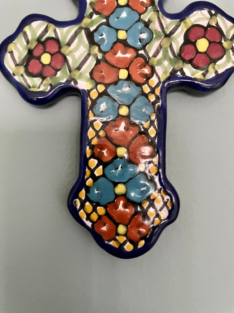 May include: A blue and white ceramic cross with a floral design. The cross is decorated with red, blue, yellow, and green flowers.