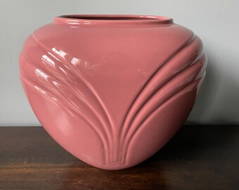 May include: A large, heart-shaped ceramic vase with a glossy, pink finish. The vase has a unique, sculpted design with curved lines.