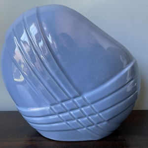 May include: A light blue ceramic vase with a geometric design. The vase is shaped like a rounded rectangle with a smooth, glossy finish.