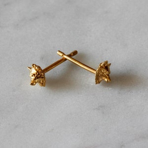 May include: A pair of gold-toned stud earrings featuring a textured, abstract design. The earrings are small and delicate.