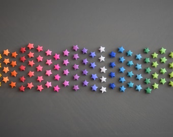 May include: A collection of origami stars arranged in a rainbow gradient against a gray background. The stars transition from yellow to red, pink, purple, blue, and green, creating a vibrant and colorful display. Ideal for crafting and decor.