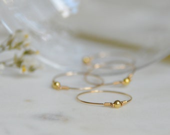 Puede incluir: Cuatro anillos de oro con una pequeña cuenta de oro en cada anillo. Los anillos están sobre una superficie blanca.