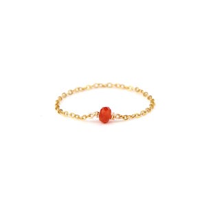 Könnte beinhalten: Ein zarter goldener Kettenring mit einem kleinen, facettierten, orangeroten Edelstein in der Mitte. Der Ring ist vor einem sauberen weißen Hintergrund platziert, der die schlichte Eleganz des Schmucks hervorhebt. Die Kette ist fein und filigran.