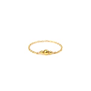 Könnte beinhalten: Ein zarter goldener Ring mit Kettengliedern und drei goldenen Perlen. Der Ring ist vor einem weißen Hintergrund platziert, was seine schlichte Eleganz unterstreicht. Der Ring ist ein feines Schmuckstück.