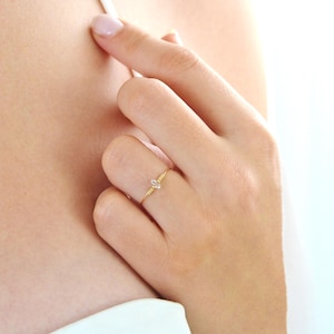 Peut inclure: Une fine bague en or avec une petite pierre précieuse transparente. La bague a un anneau fin et une pierre étincelante. La bague est portée au doigt, soulignant son design minimaliste et son éclat subtil. Un bijou délicat.