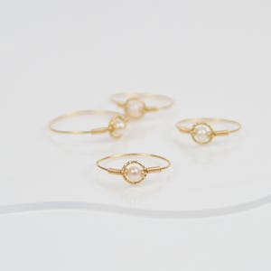 Könnte beinhalten: Vier goldene Ringe, jeder mit einer einzelnen Perle in der Mitte. Die Ringe sind zart und schlicht.