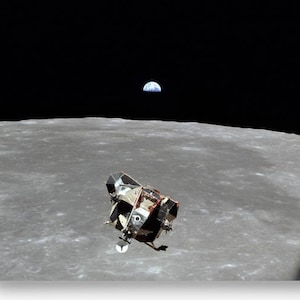 Op de afbeelding: Een zwart-witfoto van de maanlander op het oppervlak van de maan met de aarde in de verte.