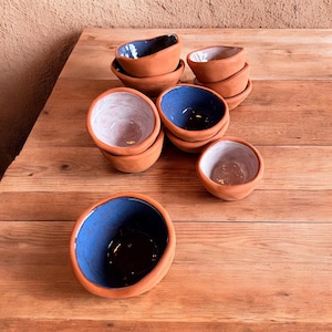 May include: A group of small terracotta bowls with blue and white glaze. The bowls are stacked and arranged on a wooden surface.