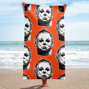 May include: An orange beach towel with a repeating pattern of a black and white illustration of Michael Myers' mask from the Halloween movies.