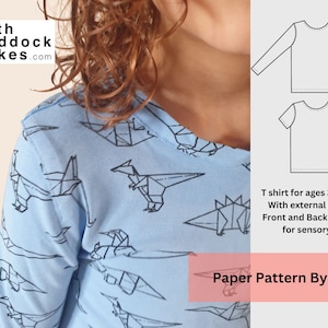 Puede incluir: Una camiseta azul de manga larga con un patrón de dinosaurio origami blanco. La camiseta es para edades de 3 a 10 años y tiene costuras externas. El texto "Ruth Maddock Makes.com" y "Paper Pattern By Post" es visible en la imagen.