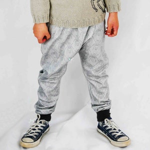 May include: Gray sweatpants with a black ant print. The sweatpants have a gathered elastic waistband and a relaxed fit. The model is wearing the sweatpants with black and blue sneakers.