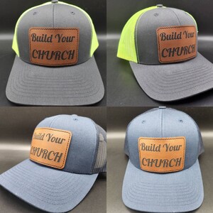May include: Four trucker hats with a black mesh back and a brown leather patch that says "Build Your Church". Two hats have a black crown and a neon green brim. Two hats have a navy blue crown and a black brim.