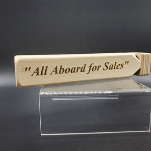 May include: A wooden whistle with the text "All Aboard for Sales" engraved on it. The whistle is sitting on a clear acrylic display stand.