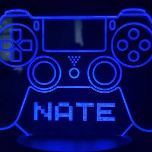 May include: A blue illuminated plastic PlayStation controller with the name "NATE" in pixelated letters on the base.