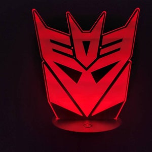 May include: A red illuminated night light shaped like the Decepticons logo from the Transformers franchise.