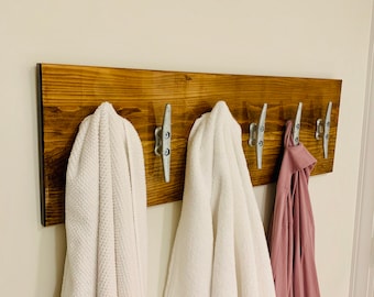 Peut inclure: Un porte-manteau mural en bois avec cinq crochets argentés. Deux serviettes blanches et une robe rose sont accrochées aux crochets.