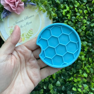 May include: A light blue silicone coaster with a honeycomb design. The coaster has a cutout for a cup.