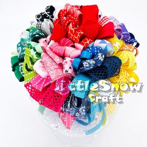 May include: A selection of colourful ribbons arranged in a spiral pattern. The ribbons are made from different materials, including satin, grosgrain, and lace. The ribbons are in a variety of colours, including red, pink, blue, green, yellow, and purple. The ribbons are arranged in a clear glass jar. The text "Little Show Craft" is visible in the image.