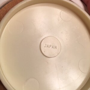 May include: Close-up of a cream-colored, circular object with the word "JAPAN" stamped in a small circle. The object has a slightly textured surface and appears to be part of a larger item.