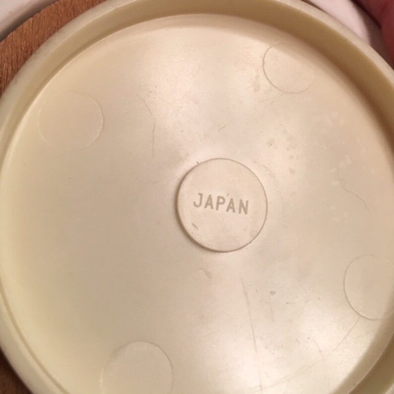 May include: Close-up of a cream-colored, circular object with the word "JAPAN" stamped in a small circle. The object has a slightly textured surface and appears to be part of a larger item.